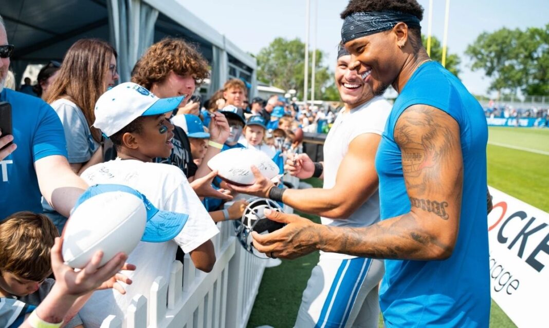 Detroit Lions players smile while signing footballs for kids during a fan event, giving young fans exclusive Cub Club experiences
