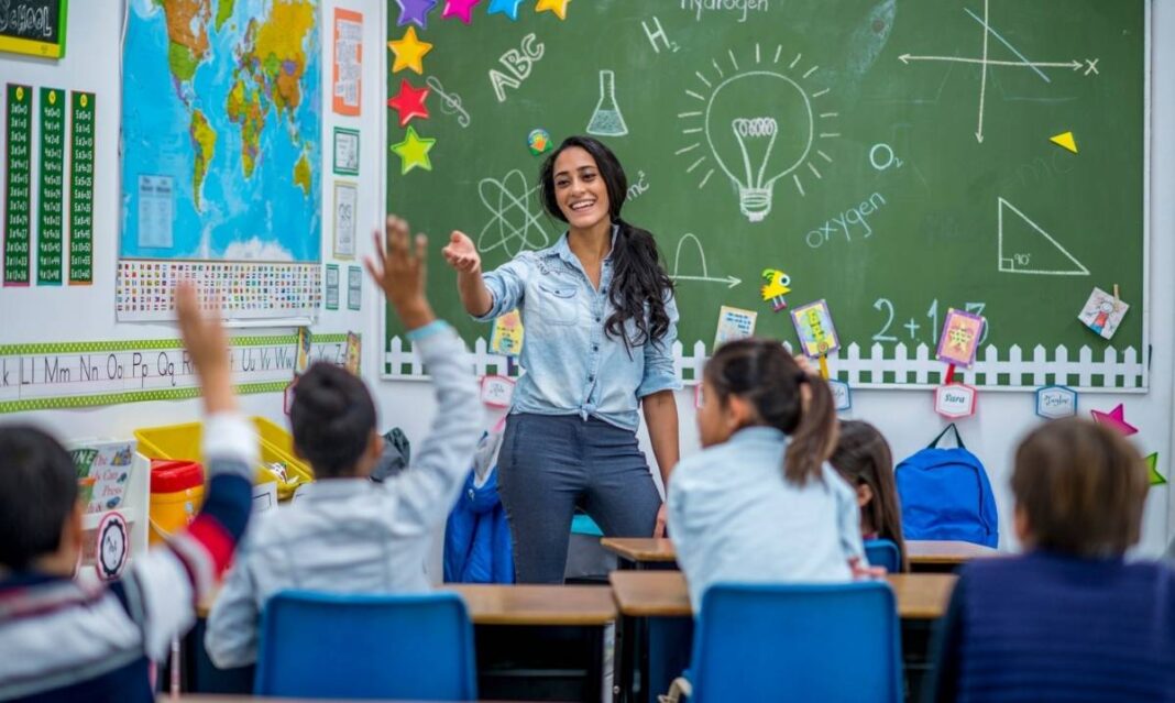 Teacher calling on students raising their hands in a classroom, representing Detroit Public Schools board meeting updates on staffing and performance.