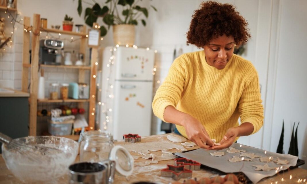 Parent bakes Christmas cookies at home with dough and cutters on the table for an easy holiday recipe kids can help make.