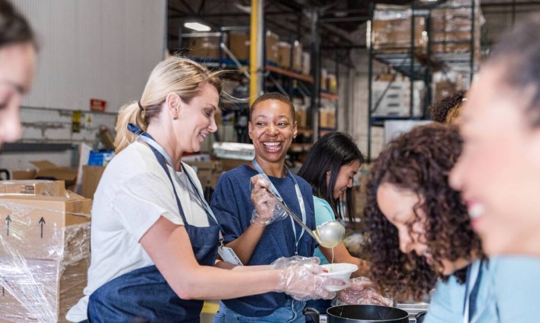Volunteers smiling while serving food at a community event, representing the Southeast Michigan Ford Dealers and Forgotten Harvest food drive.