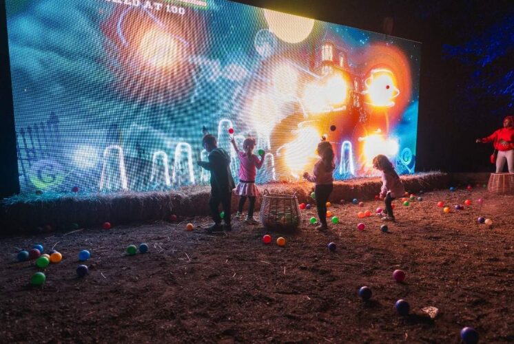 Kids play in front of a glowing interactive light display at Glenlore Trails Witching Hour, a family-friendly Halloween event in Michigan.