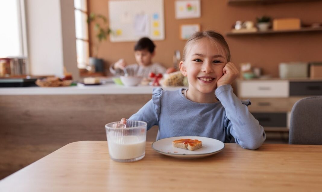 Smiling child sitting at a kitchen table with a glass of milk and toast, showing a healthy after-school snack.