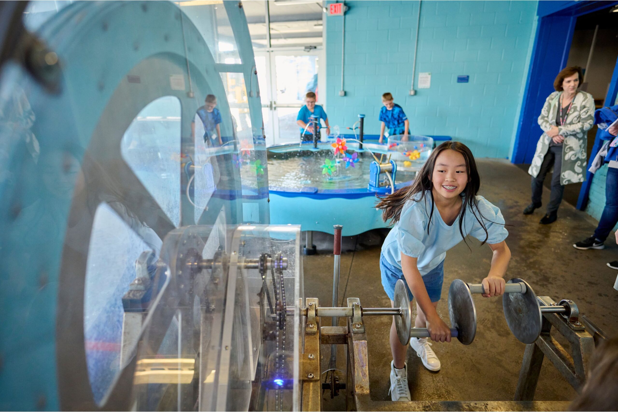 A girl smiles while turning wheels at the water exhibit inside Impression 5 Science Center in Lansing with other kids exploring nearby.