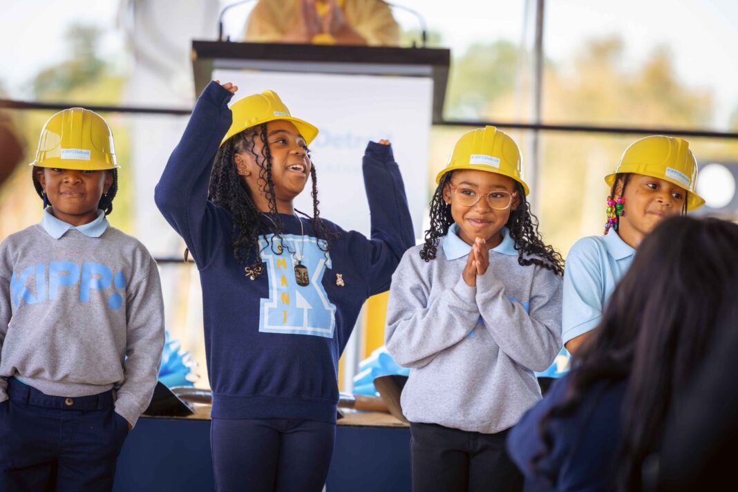 KIPP Detroit Imani Academy students wear yellow hard hats and smile on stage during the new Gardenview campus groundbreaking event.
