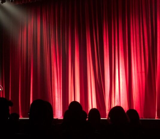 Rudolph the Red-Nosed Reindeer: The Musical Audience waits in front of red stage curtains before a live holiday musical performance of Rudolph the Red-Nosed Reindeer.