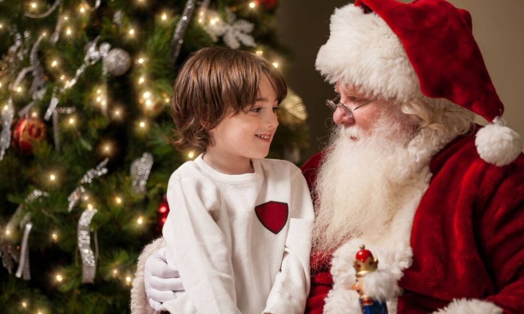 Child sitting on Santa’s lap smiling beside a Christmas tree, representing Santa meet-and-greet events for families in metro Detroit.