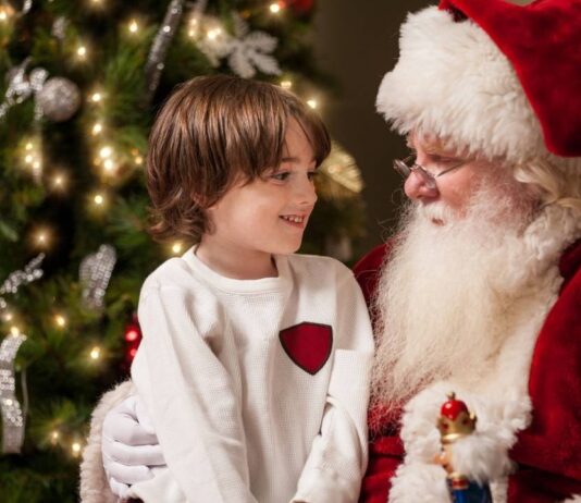 Santa at Savas Child sitting on Santa’s lap smiling beside a Christmas tree, representing Santa meet-and-greet events for families in metro Detroit.