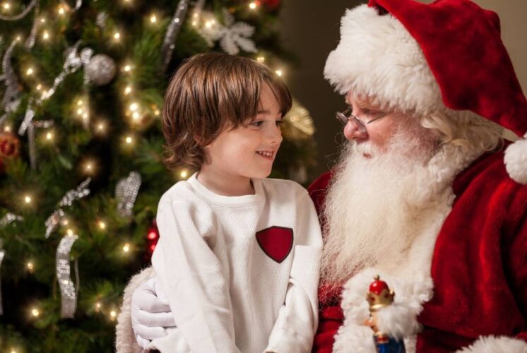 Child sitting on Santa’s lap smiling beside a Christmas tree, representing Santa meet-and-greet events for families in metro Detroit.