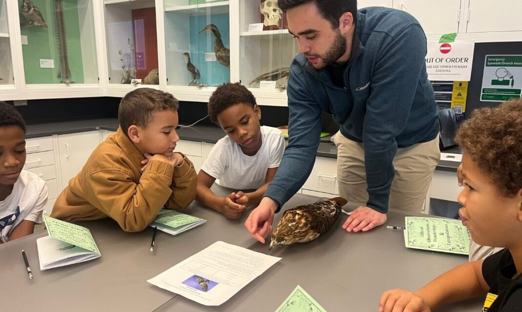 Teacher guides elementary students in a science classroom, examining a bird specimen during a hands-on learning activity