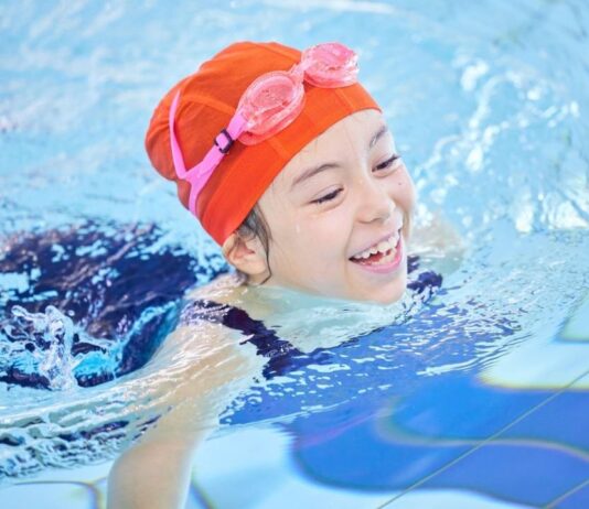 Child smiling while swimming in a pool during the Swim with Santa event at Summit on the Park in Canton with holiday fun for families