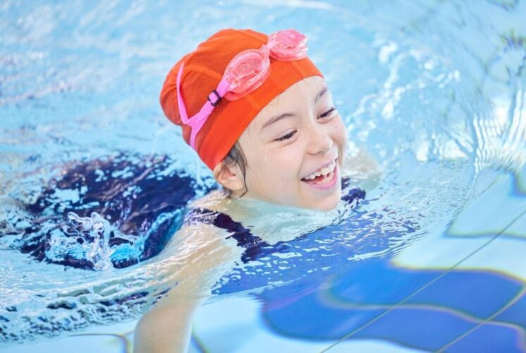 Child smiling while swimming in a pool during the Swim with Santa event at Summit on the Park in Canton with holiday fun for families