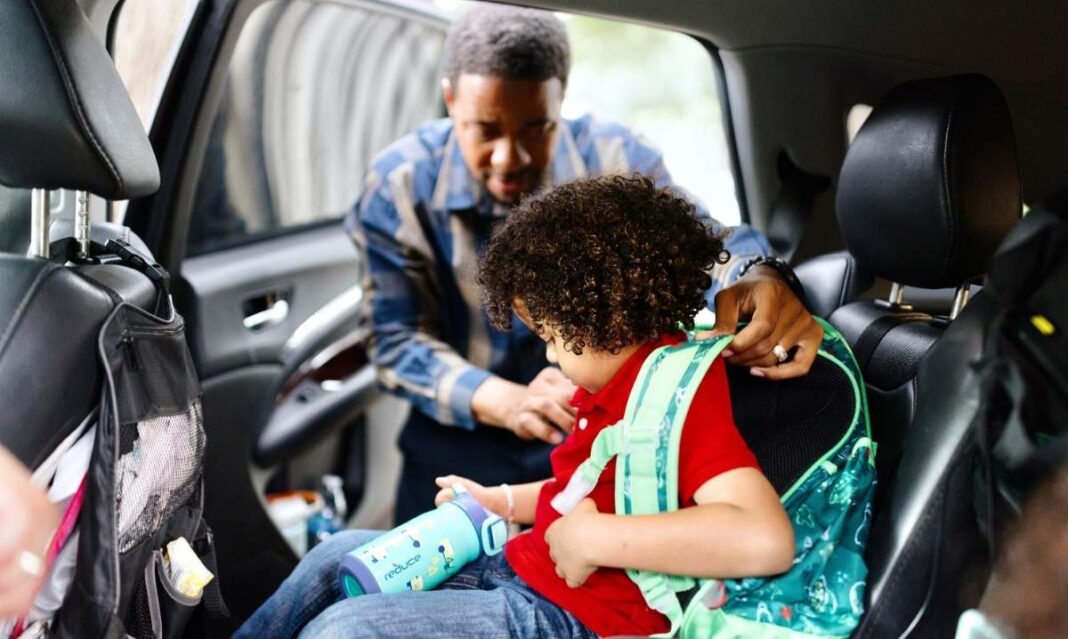 Parent helping child with backpack and car seat in the backseat, representing Target’s car seat trade-in and recycling program for families.