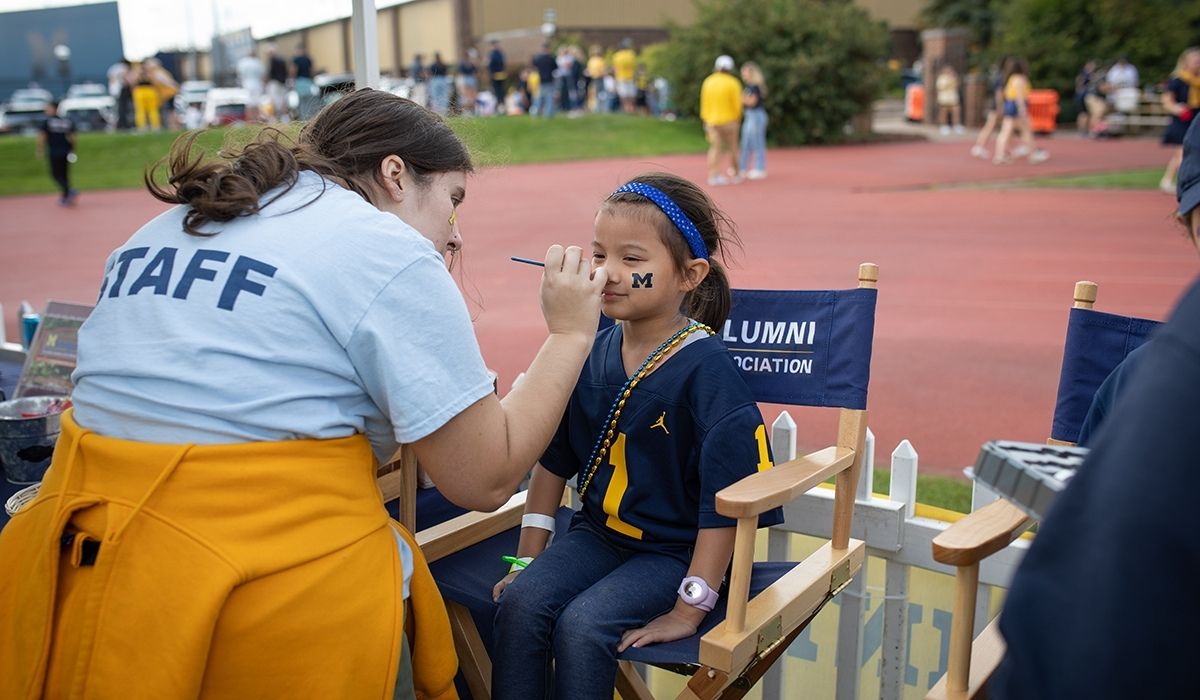 A young Michigan fan gets her face painted with the block M logo during a University of Michigan football game alumni event.