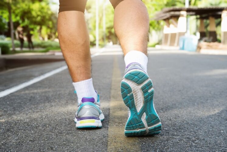 Close-up of a person walking in athletic shoes on a paved road, representing outdoor fitness, health walks, and community walk events.