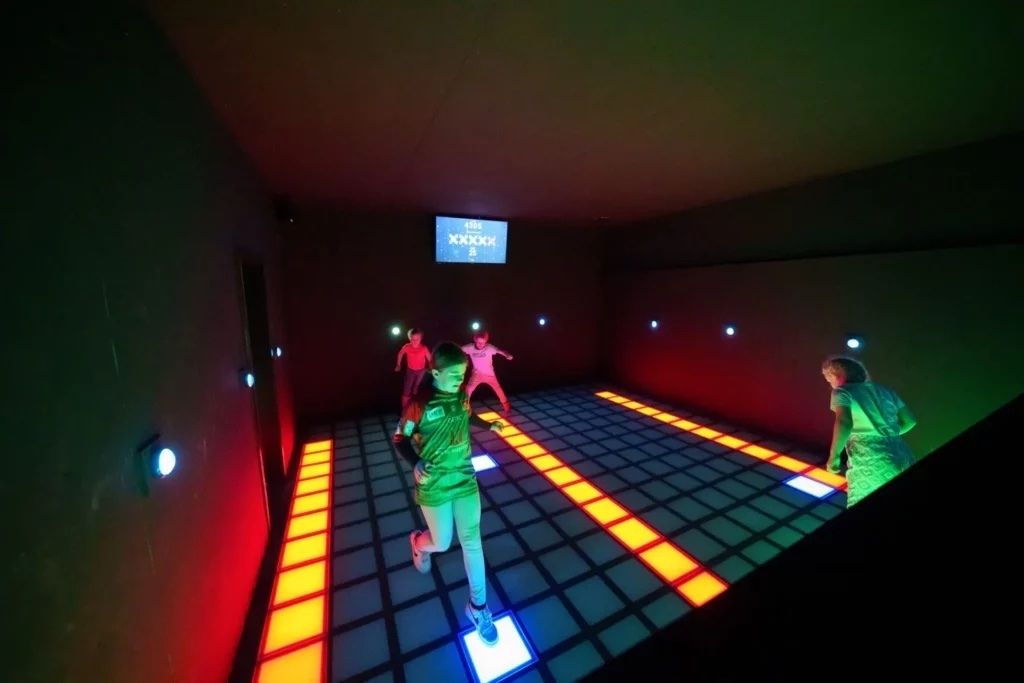 Kids play on a colorful light-up floor game at BIG Best in Games arcade in metro Detroit during an indoor play session.