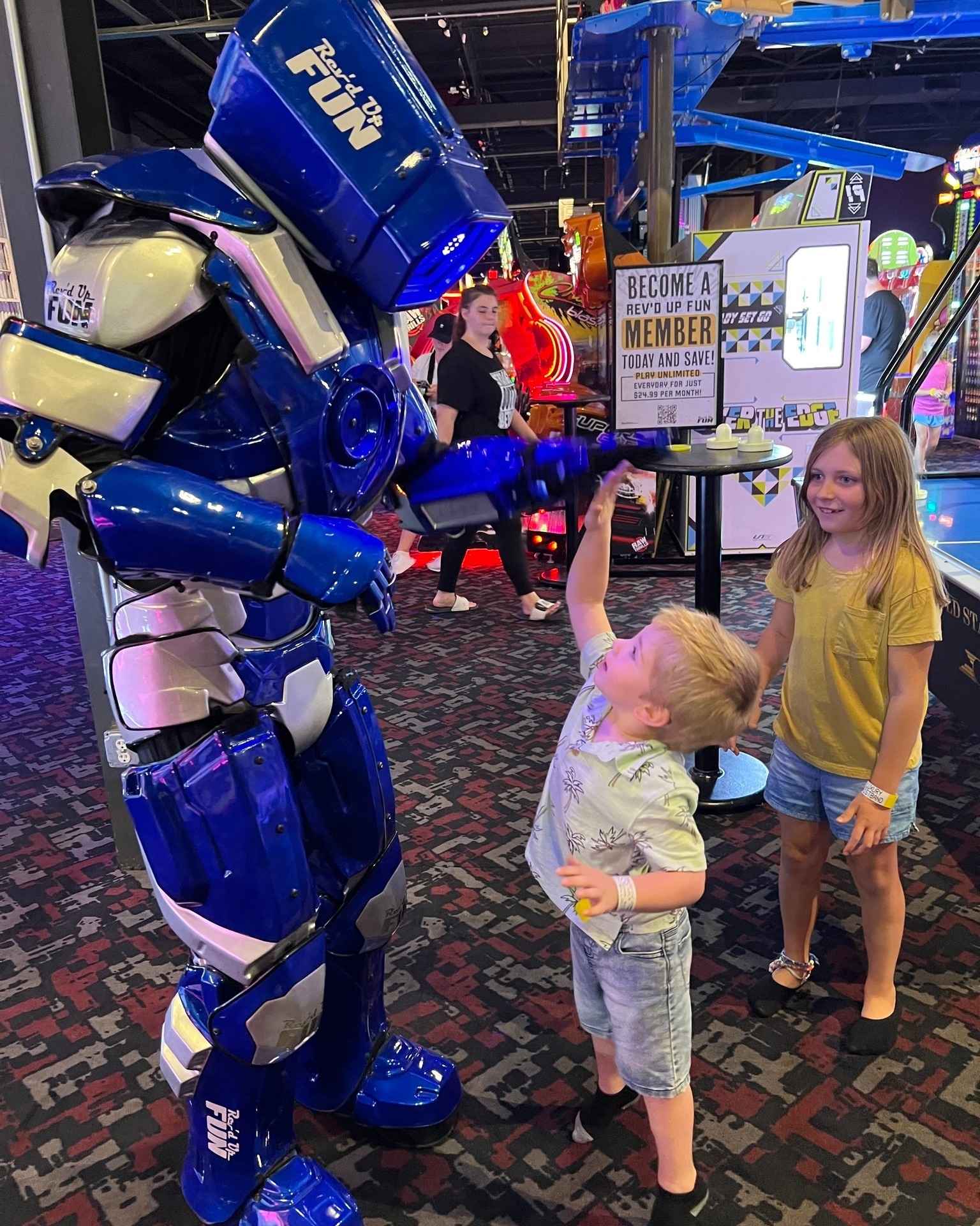Kids meet Axle the robot mascot at Rev’d Up Fun arcade, posing for a photo and enjoying interactive family entertainment.