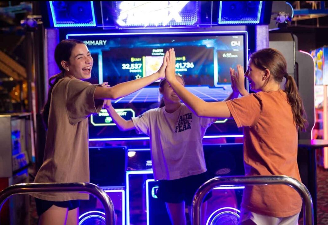 Three girls laugh and high-five after playing a dance game at Rev’d Up Fun arcade in metro Detroit.
