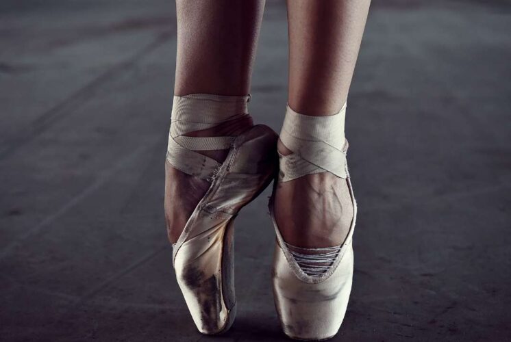 Close-up of ballet dancer's feet in worn pointe shoes poised on tips, highlighting dance performance for Las Posadas celebration event.