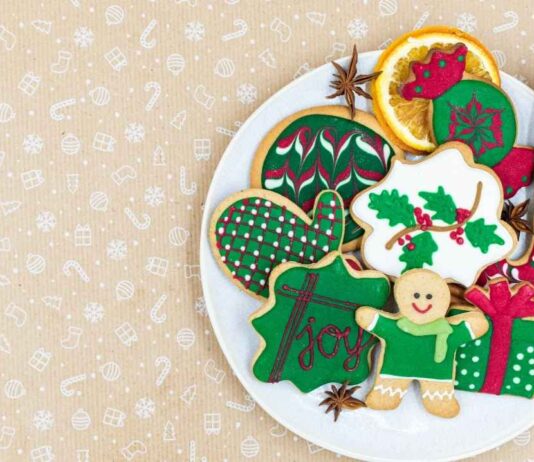 A festive plate of decorated Christmas cookies with a gingerbread person, holly, a present, and holiday symbols on a light background, celebrating holiday events.