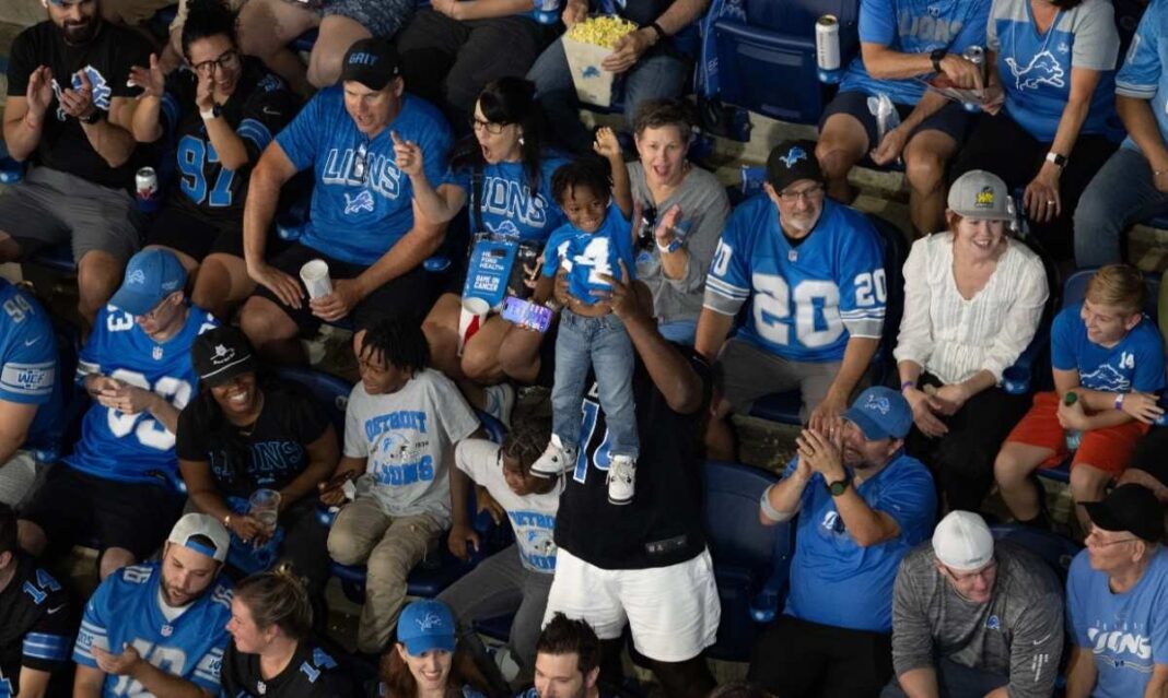 Detroit Lions fans cheer with kids during a family-friendly football game at Ford Field, showing Detroit’s team spirit and game day fun.