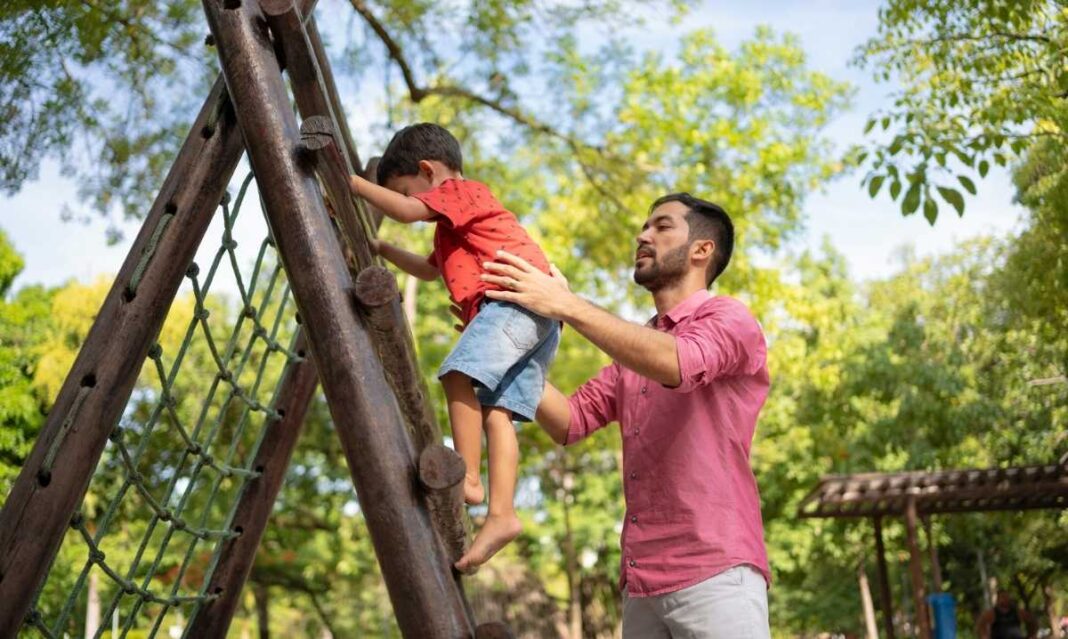 Dad helping young child climb wooden structure at Fort Fraser in Steffens Park Fraser Michigan during a sunny fall day