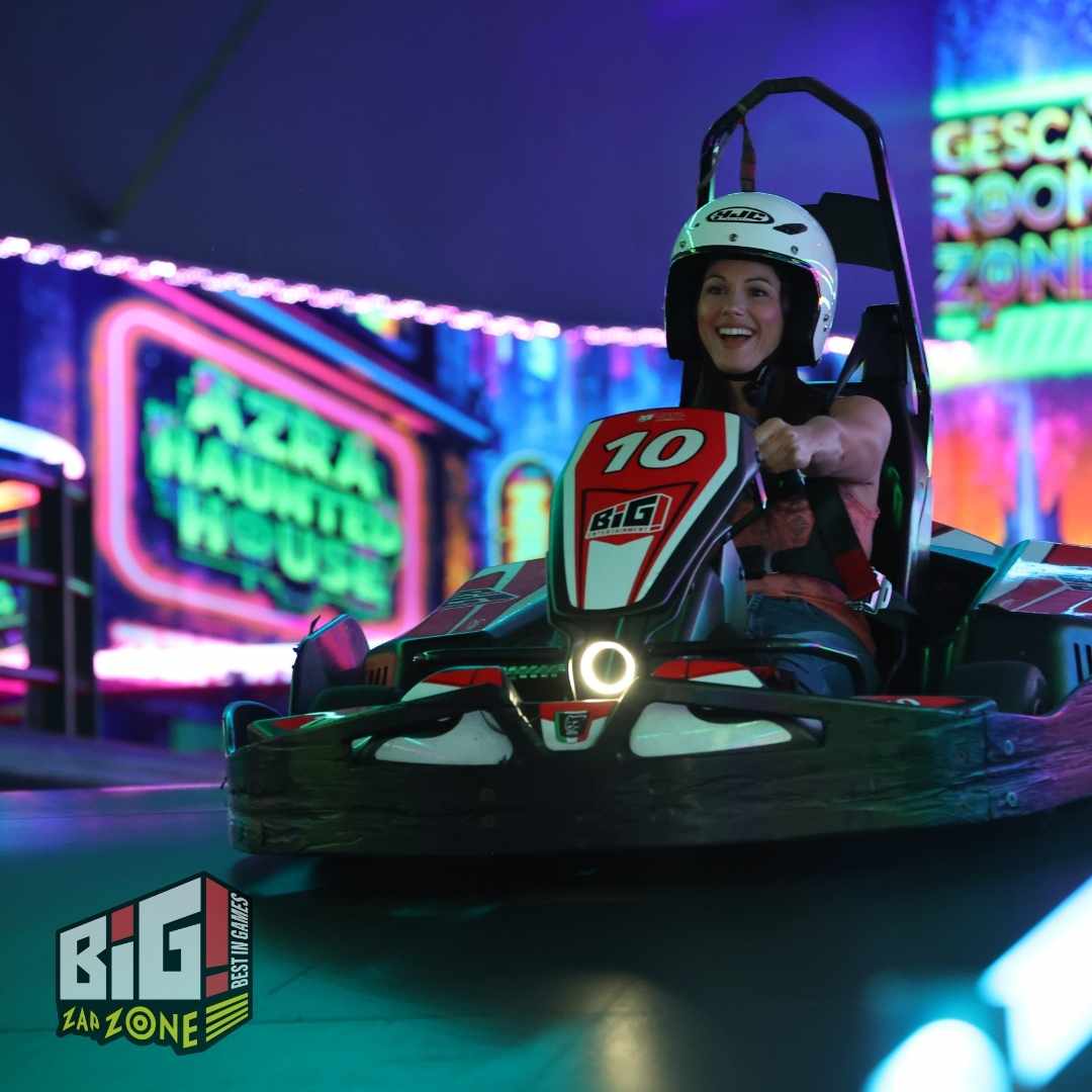 A woman drives a go-kart at Big Zap Zone family fun center, smiling as she races under neon lights during the indoor karting event.