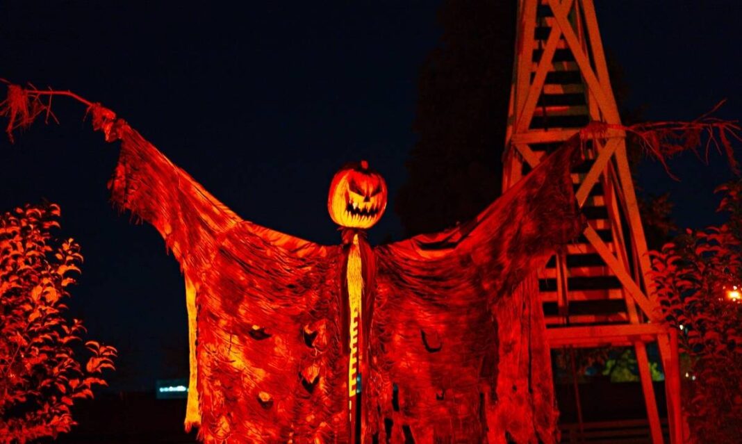A glowing scarecrow with a carved pumpkin head and tattered cloak lit in red at Halloween in Greenfield Village.