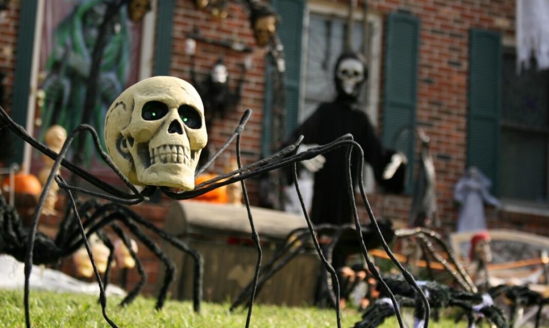 Skeleton spider decoration on a front lawn with spooky Halloween props and skeletons, representing Halloween yard displays in metro Detroit.