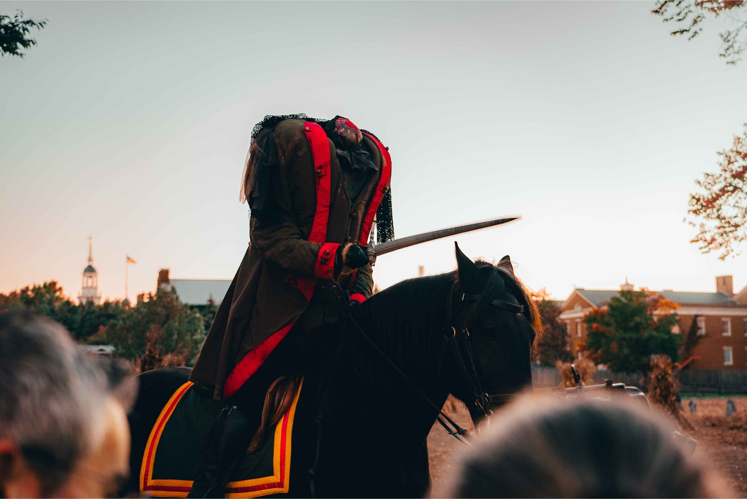 A headless horseman holding a sword rides a black horse at Greenfield Village during Halloween festivities.