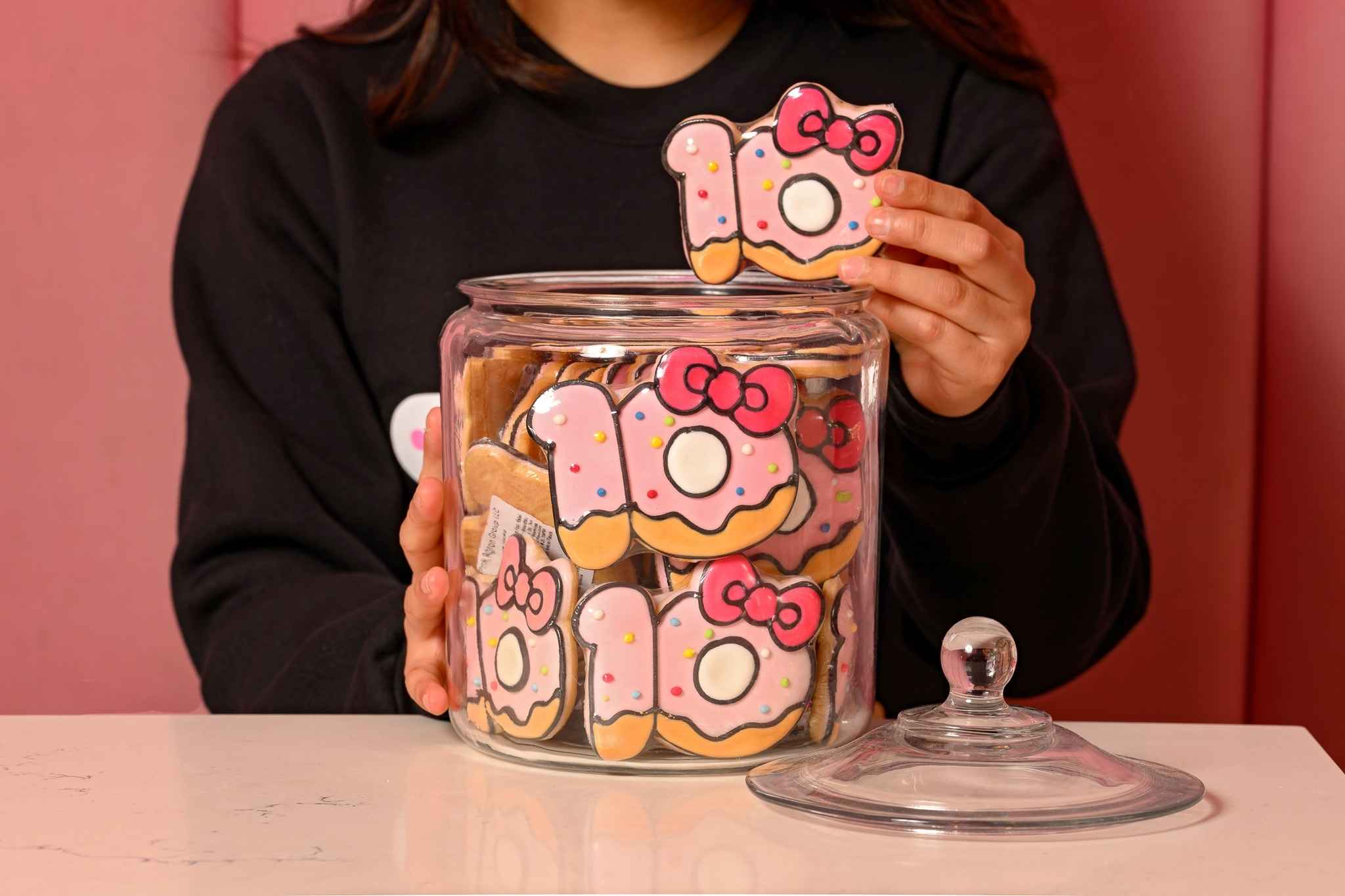 A person holds Hello Kitty Cafe 10th anniversary cookies in a jar, featuring pink icing and bows, at Twelve Oaks Mall in Novi.