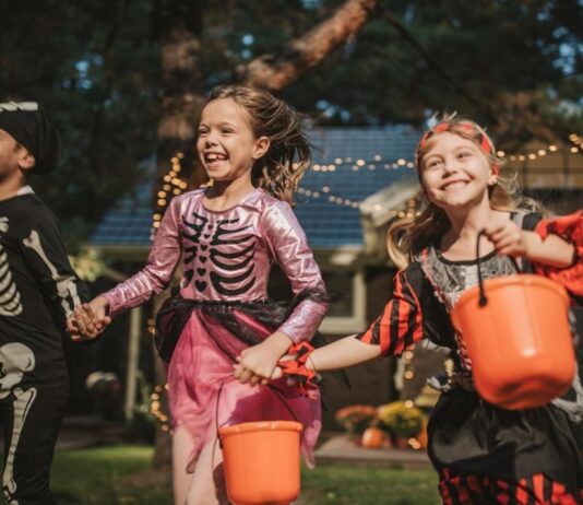 Kids dressed in Halloween costumes run outdoors holding buckets during Hoots, Howls, and Haunted Trails at Greenmead Historical Park in Livonia.