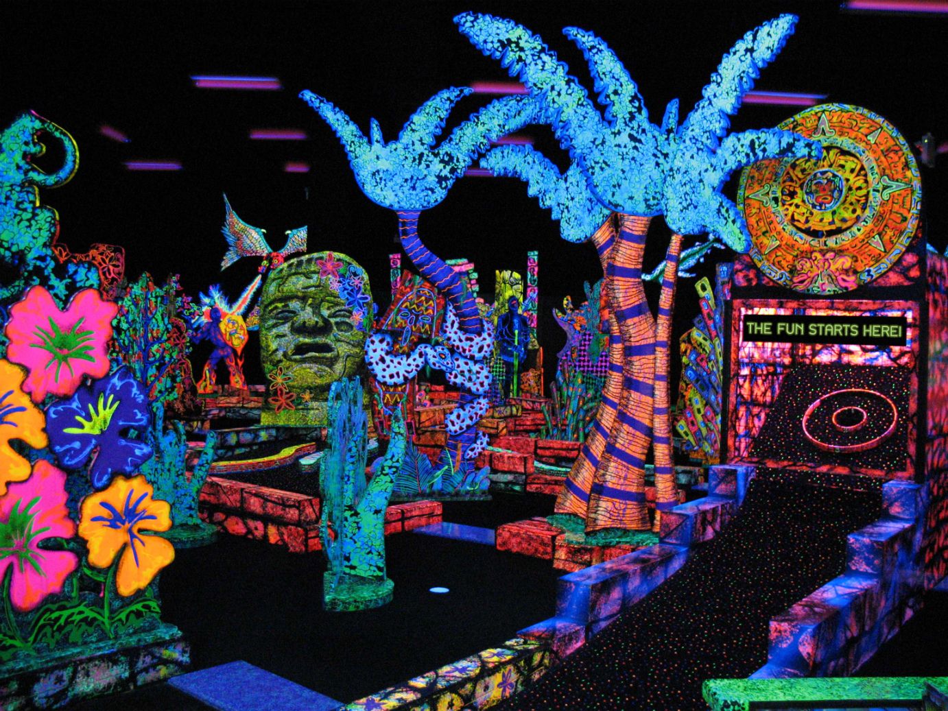 Glow-in-the-dark mini golf course at Putting Edge in southeast Michigan with neon palm trees, murals, and bright family fun decor.