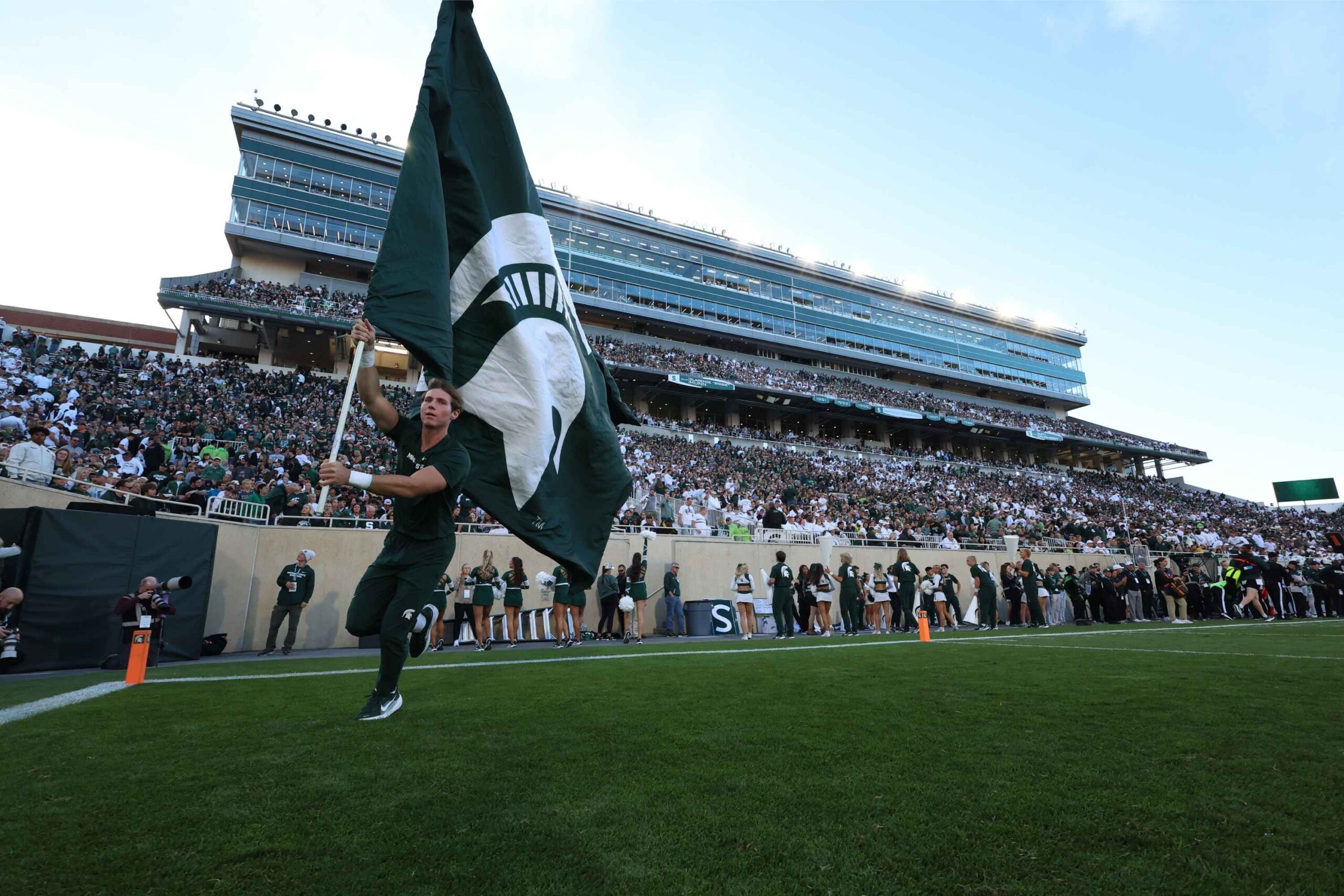Michigan State University cheerleader runs with the Spartan flag on the field during a home football game at Spartan Stadium in East Lansing.