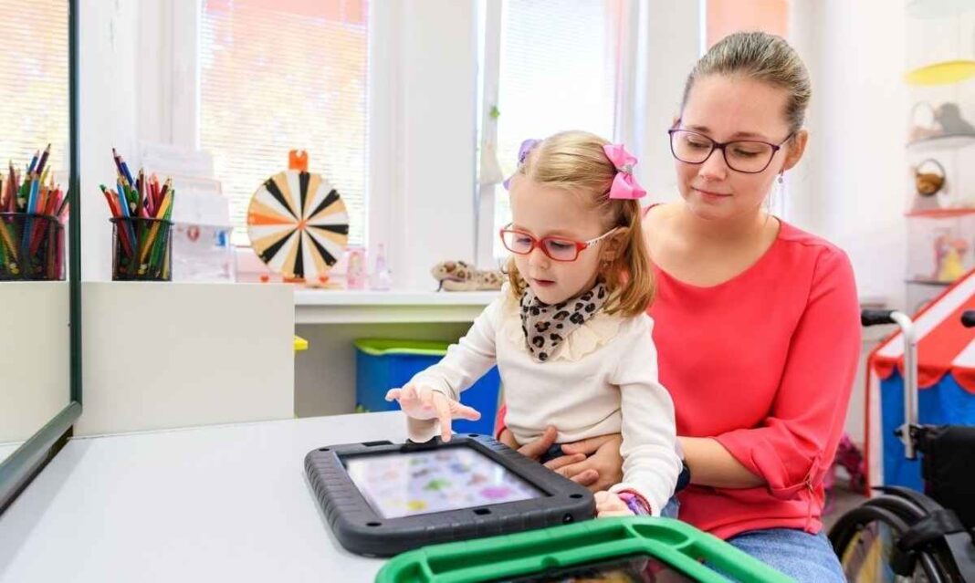 Child using a digital AAC device with therapist support during speech and ABA therapy for autism in metro Detroit