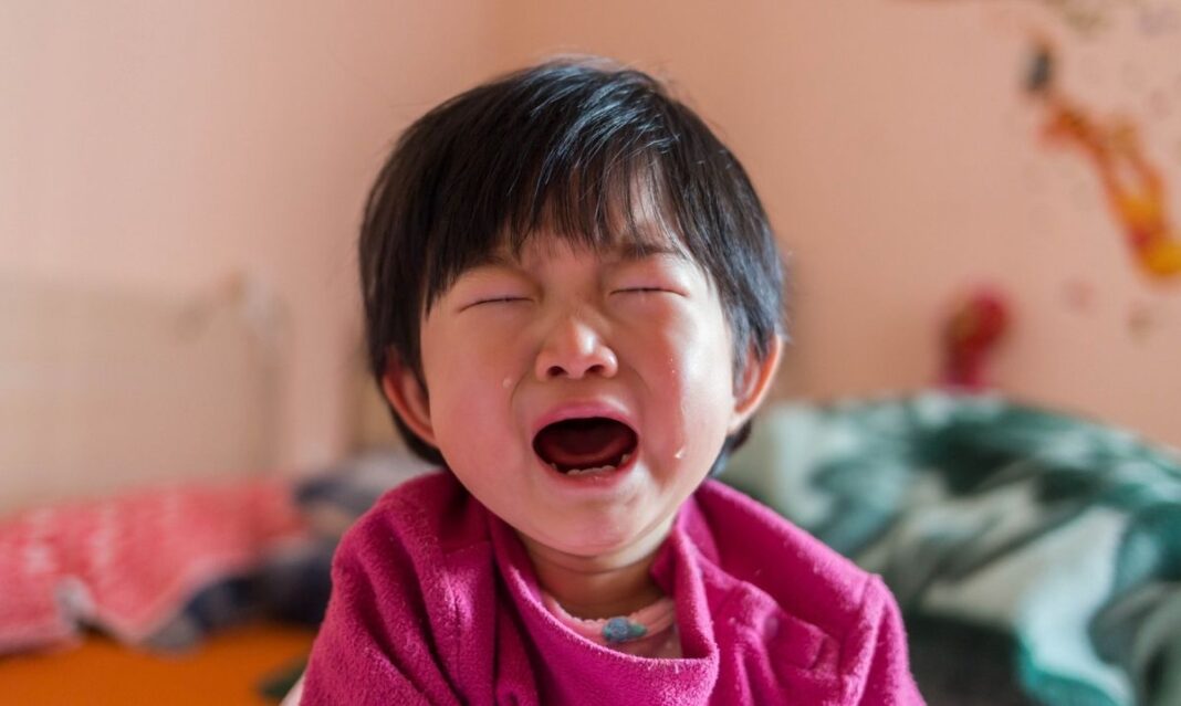A young child wakes up crying in bed, showing distress and tears, illustrating why kids wake up upset at night.