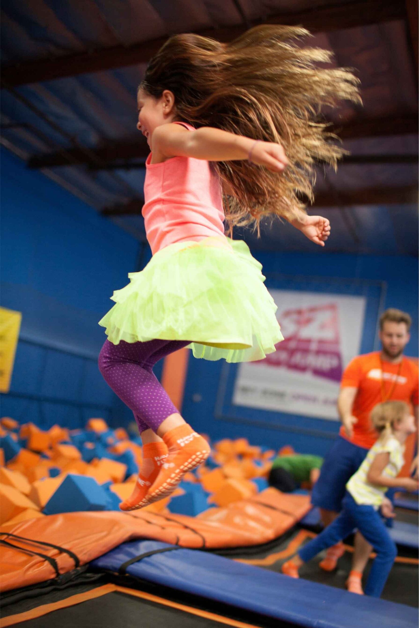 Young girl wearing a tutu jumps high on a trampoline at Sky Zone indoor play park in Michigan having fun with friends.