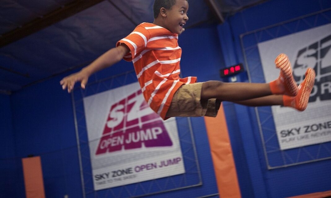 Smiling boy jumps high at Sky Zone trampoline park in Michigan during indoor play time full of fun and energy.