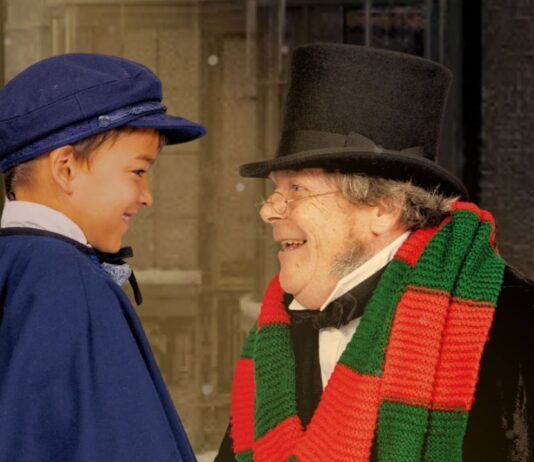 A Christmas Carol Meadow Brook Theatre holiday scene showing an older man in a top hat smiling at a young boy in costume during the classic show