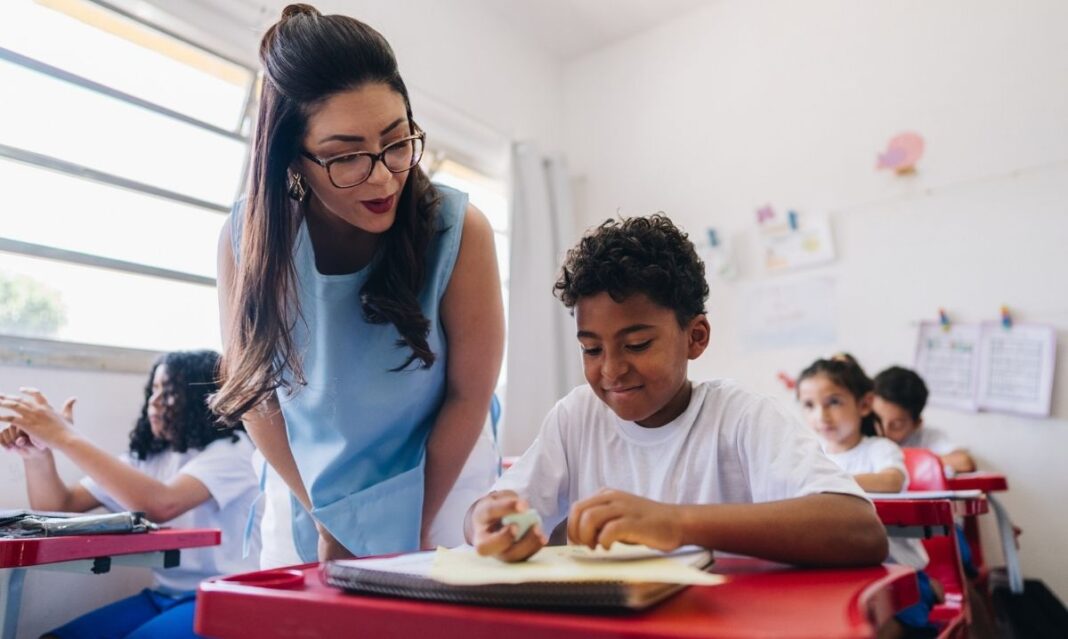 Teacher helps elementary student during class at Birmingham Public Schools, highlighting strong academics and student support.