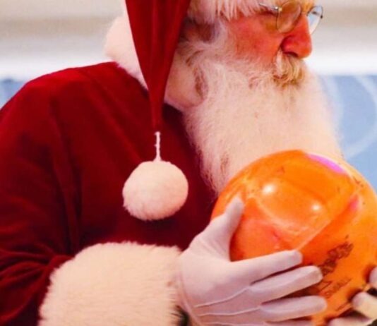 Santa holding a bowling ball at Bowl With Santa Wonderland Lanes during a festive family bowling event