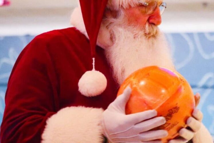 Santa holding a bowling ball at Bowl With Santa Wonderland Lanes during a festive family bowling event