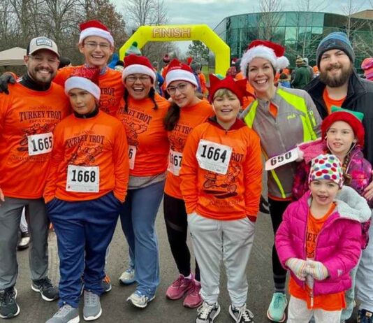 Families in bright orange shirts and Santa hats smile after finishing the Canton Turkey Trot at Summit on the Park on Thanksgiving morning.