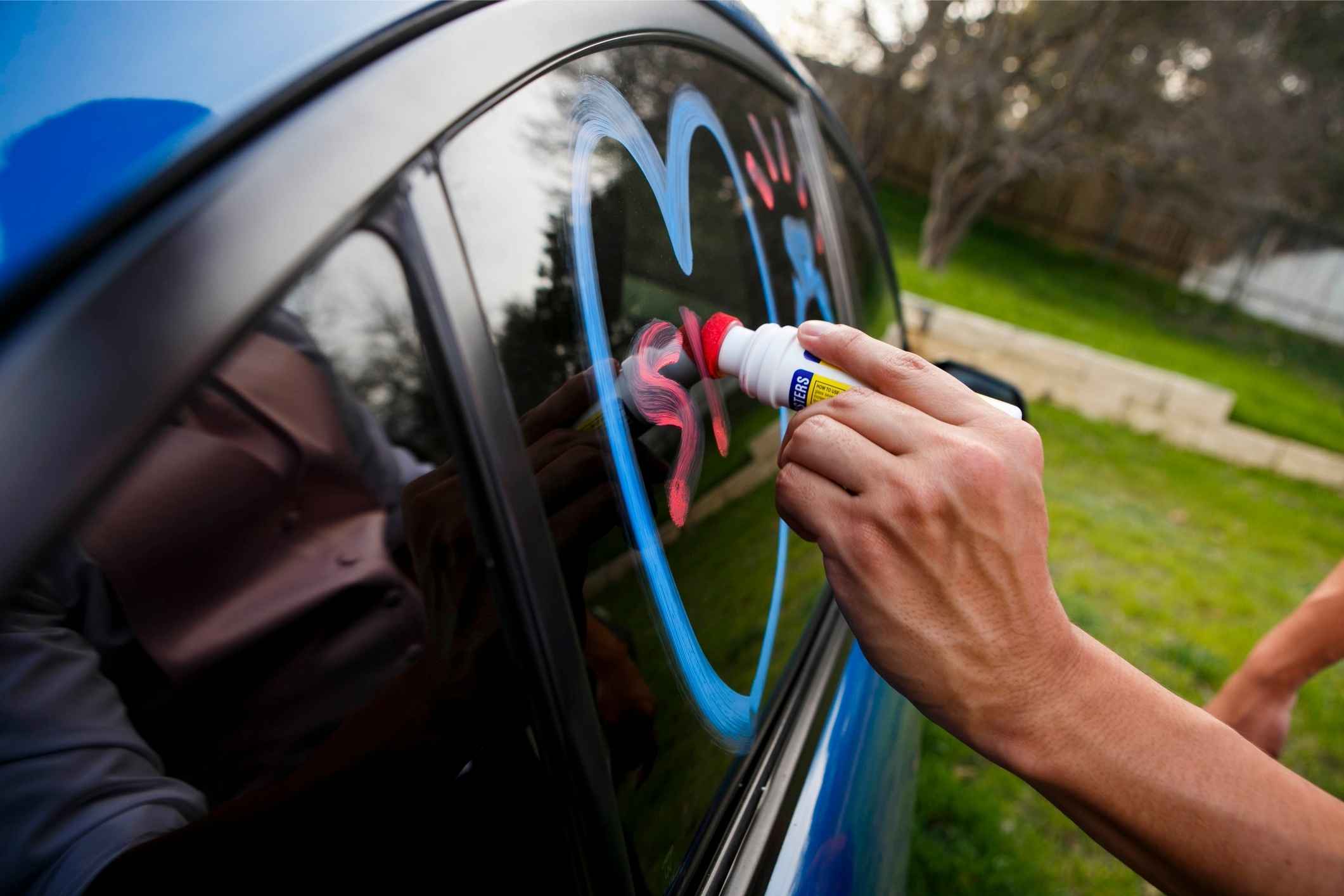 A person decorates a car window with blue and red paint, showing Detroit Lions pride through fun family SUV decorations for game day.