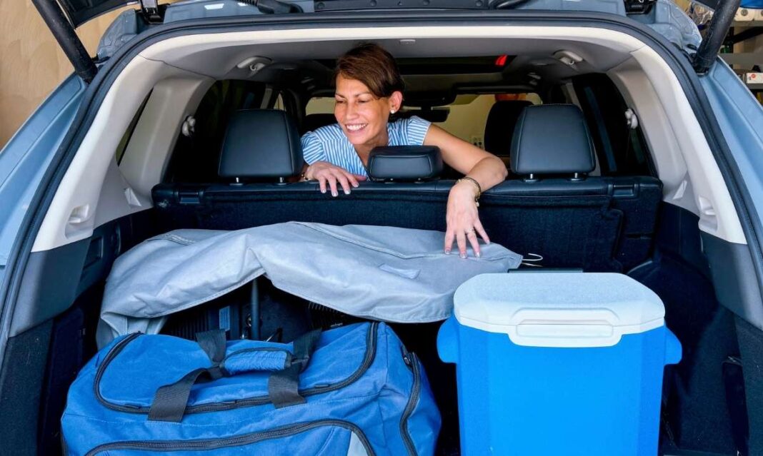 A woman loads blue and silver gear and a cooler into her SUV trunk, preparing Detroit Lions decorations for a family game day.