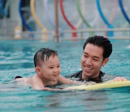Family swim Goldfish Swim School moment with a parent helping a young child practice swimming in a warm pool during open swim time