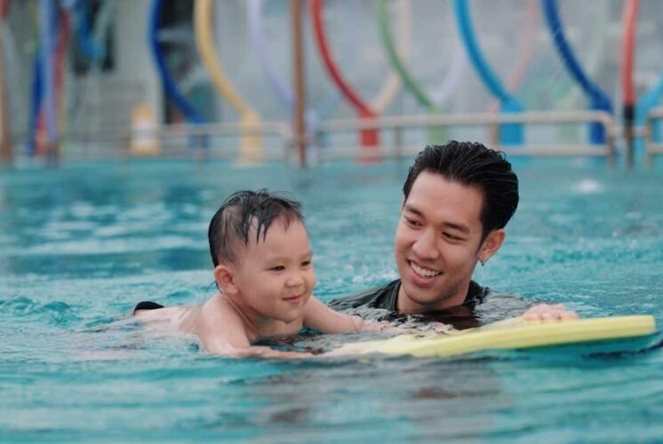 Family swim Goldfish Swim School moment with a parent helping a young child practice swimming in a warm pool during open swim time