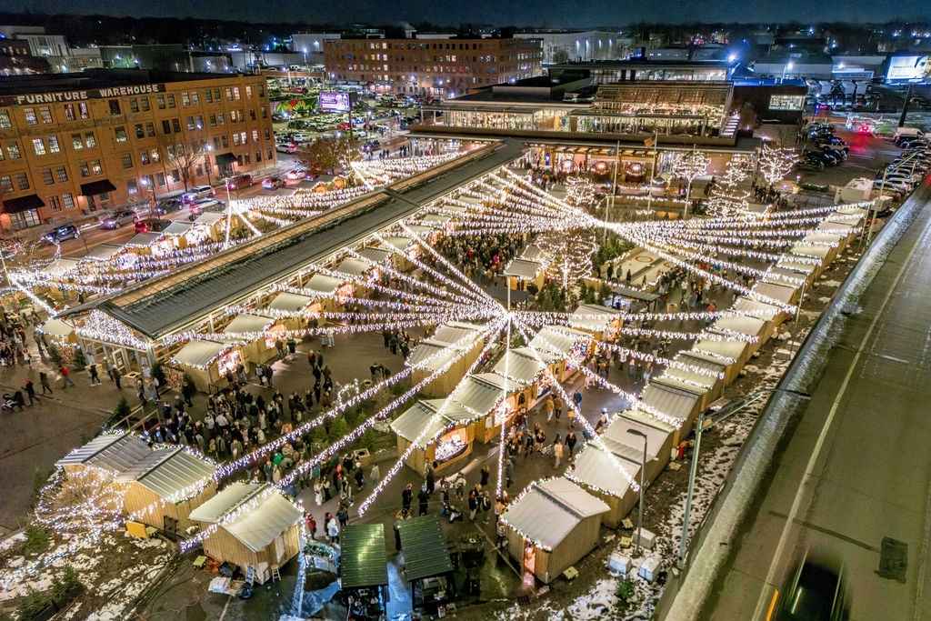 Aerial view of the Grand Rapids Christkindl Markt with glowing Christmas lights, festive vendor stalls and families exploring the holiday market at night.