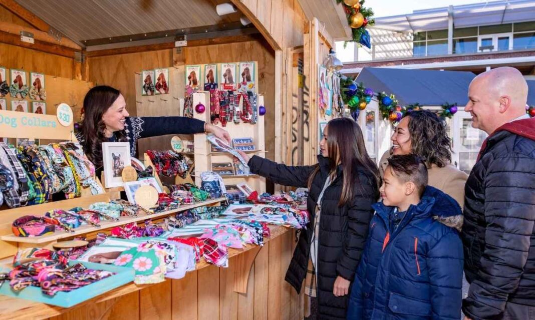 A family shops for dog collars at a festive vendor stall at the Grand Rapids Christkindl Markt during the Christmas season.