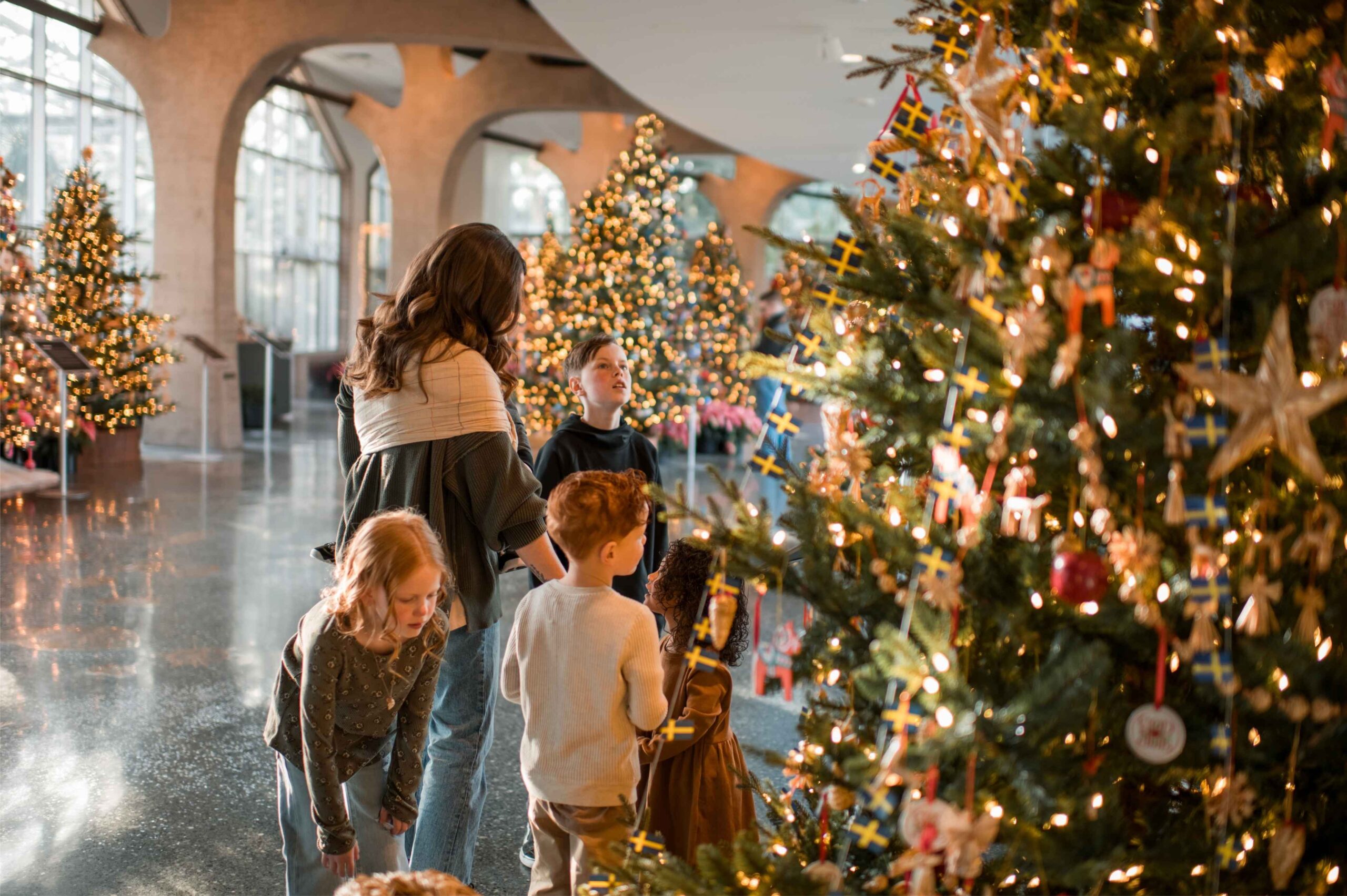 Families explore decorated Christmas trees at Frederik Meijer Gardens in Grand Rapids during the holiday season, enjoying festive lights and cultural displays.