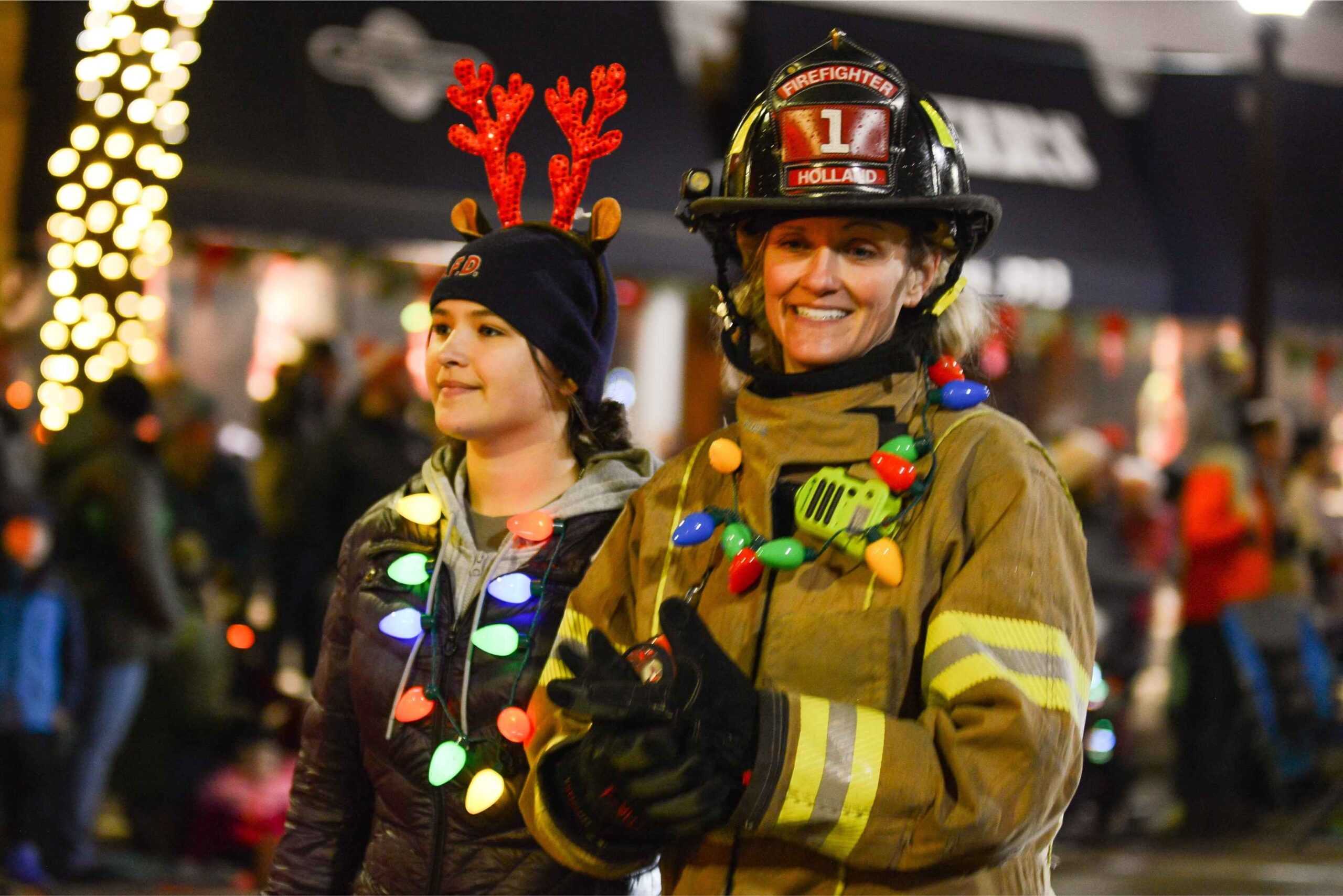A Holland firefighter and parade volunteer wearing Christmas lights participate in a festive Holland Michigan holiday event with families watching.